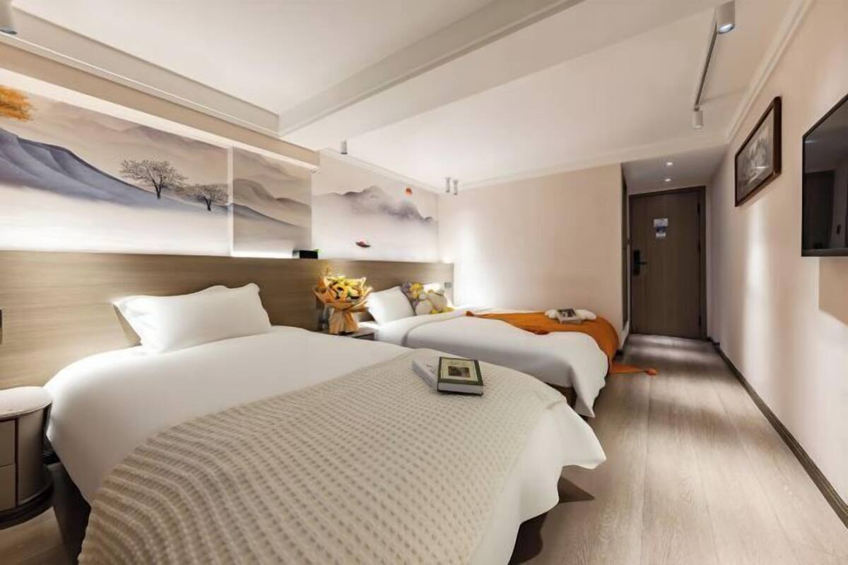 A hotel room with two beds, a TV, a painting on the wall, and a wooden floor.