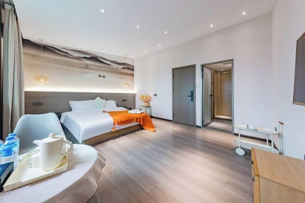 A modern hotel room with a large bed, a seating area, a small table with a tray, and a door leading to another room.