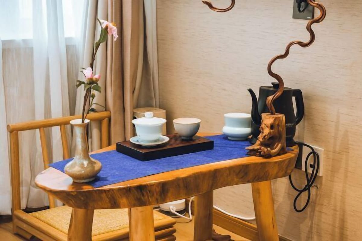 A wooden table with a blue cloth, a vase with flowers, and a coffee maker.