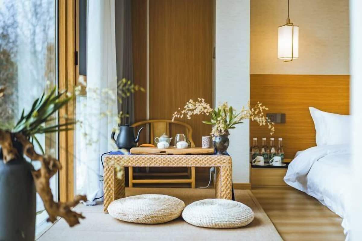 A hotel room with a bed, a bedside table with a vase of flowers, a wooden headboard, and a hanging light fixture.