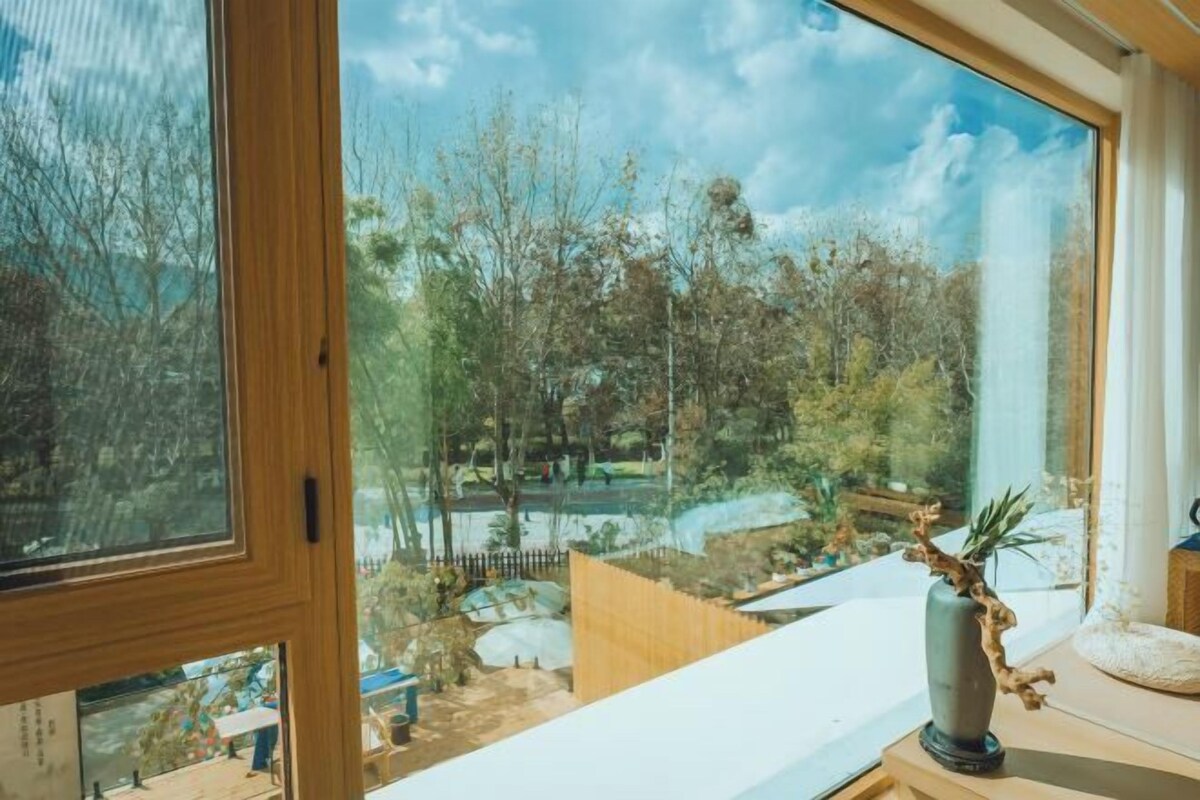 A room with a large window overlooking a garden with trees and a pathway.