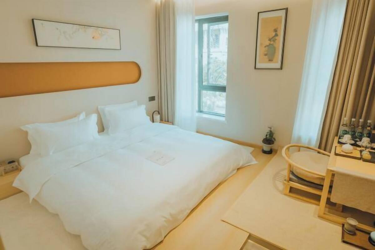 A hotel room with a bed, bedside table, and a window.