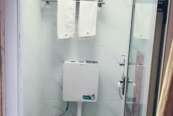 A bathroom with a glass shower enclosure, a white toilet, and two white towels hanging on a rack.