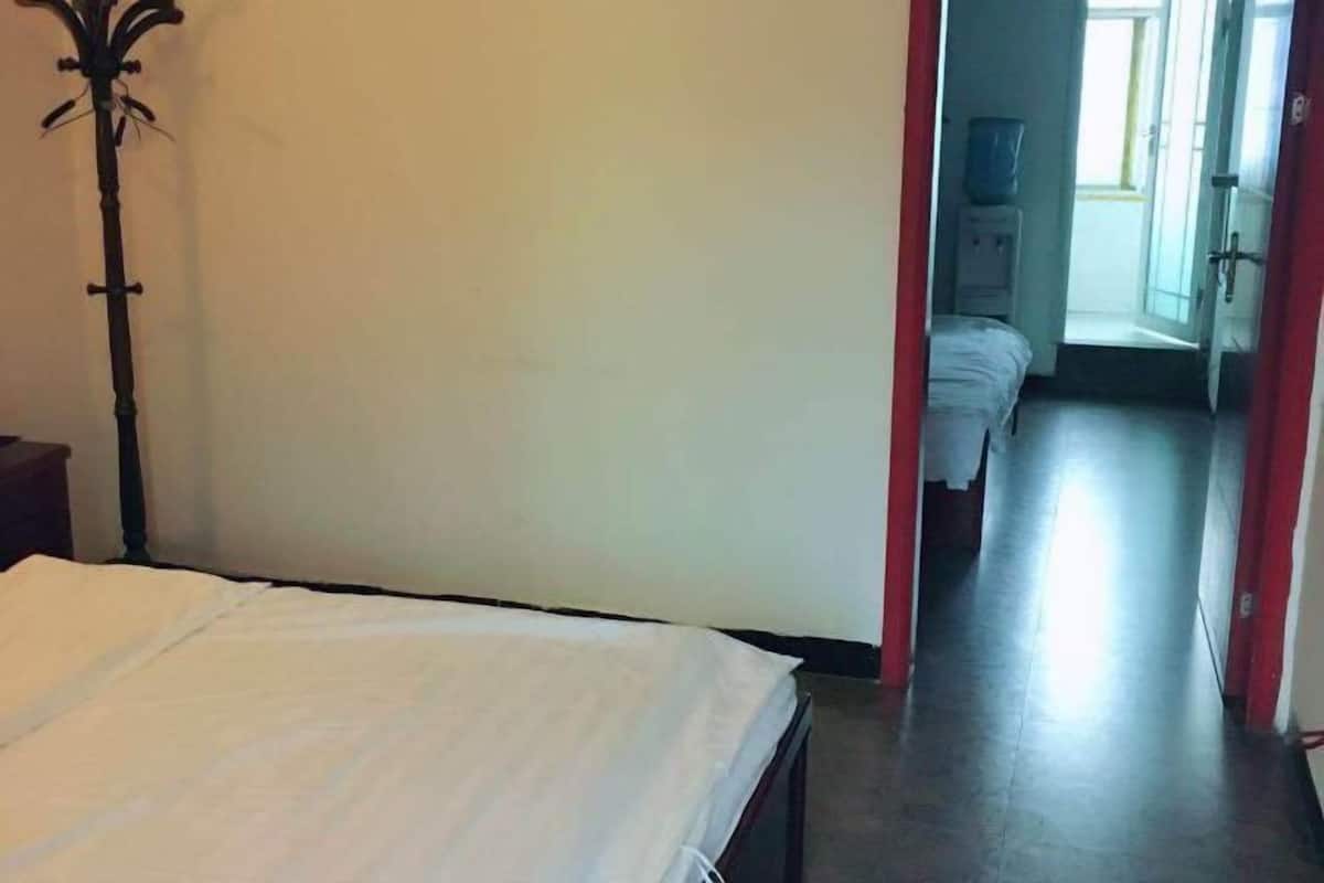 Ein Schlafzimmer mit Bett, Kleiderständer, Nachttisch und einem zur nächsten Tür führenden Flur.
