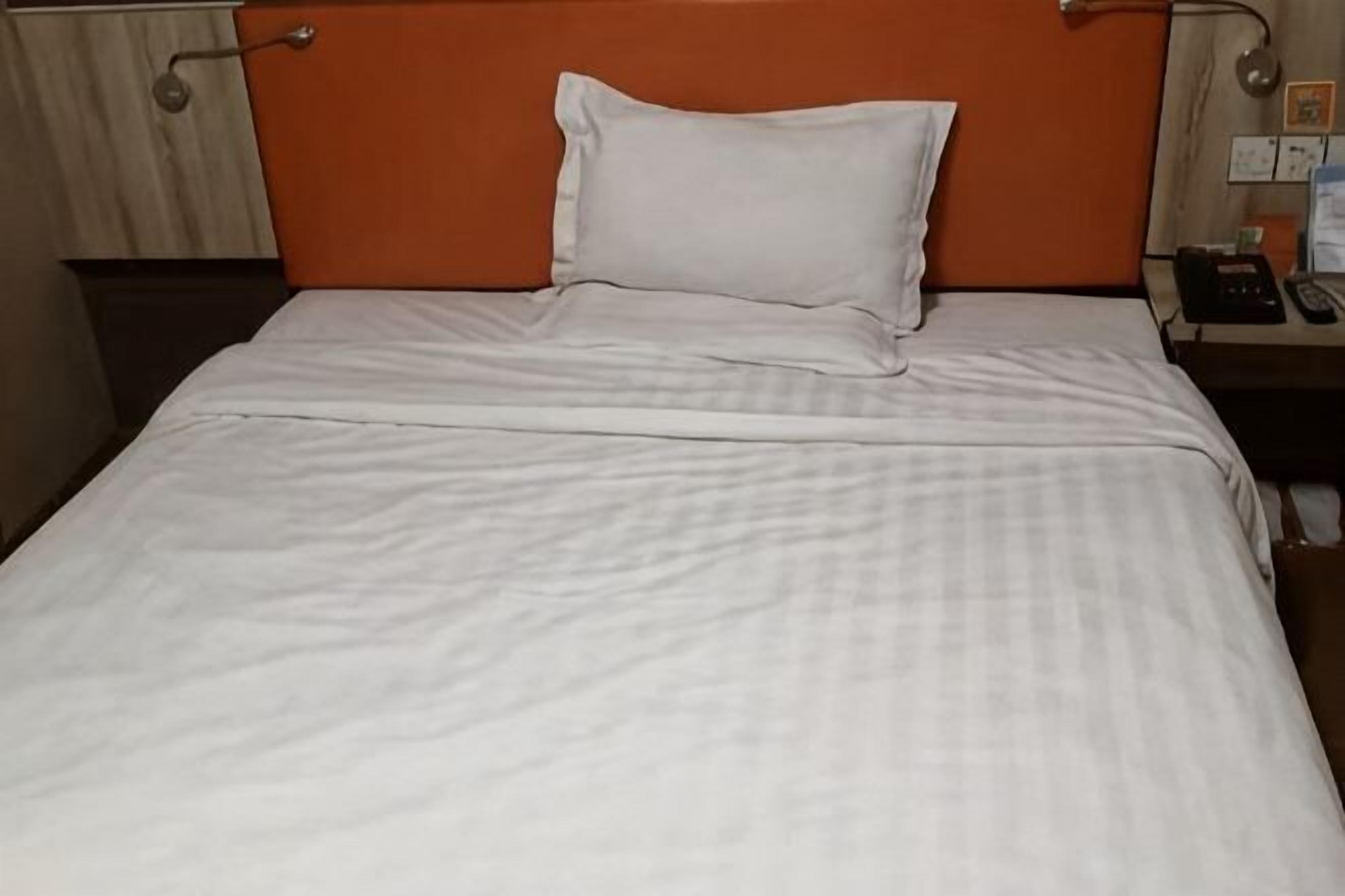 Een bed met een witte sprei en één wit kussen.