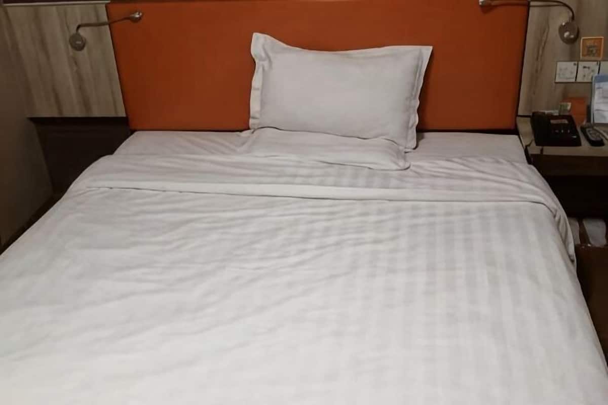 A bed with a white bedspread and a single white pillow.