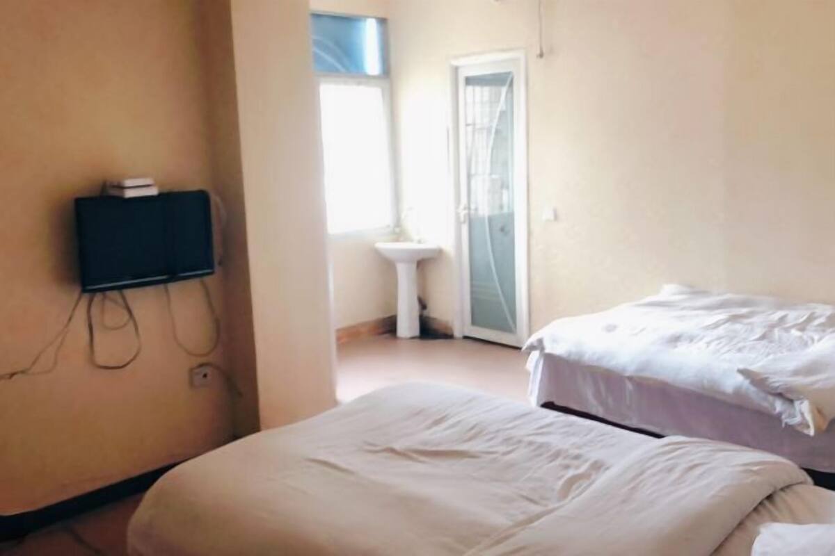 Ein Zimmer mit zwei Betten, einem kleinen weißen Waschbecken und einem an der Wand befestigten Fernseher.