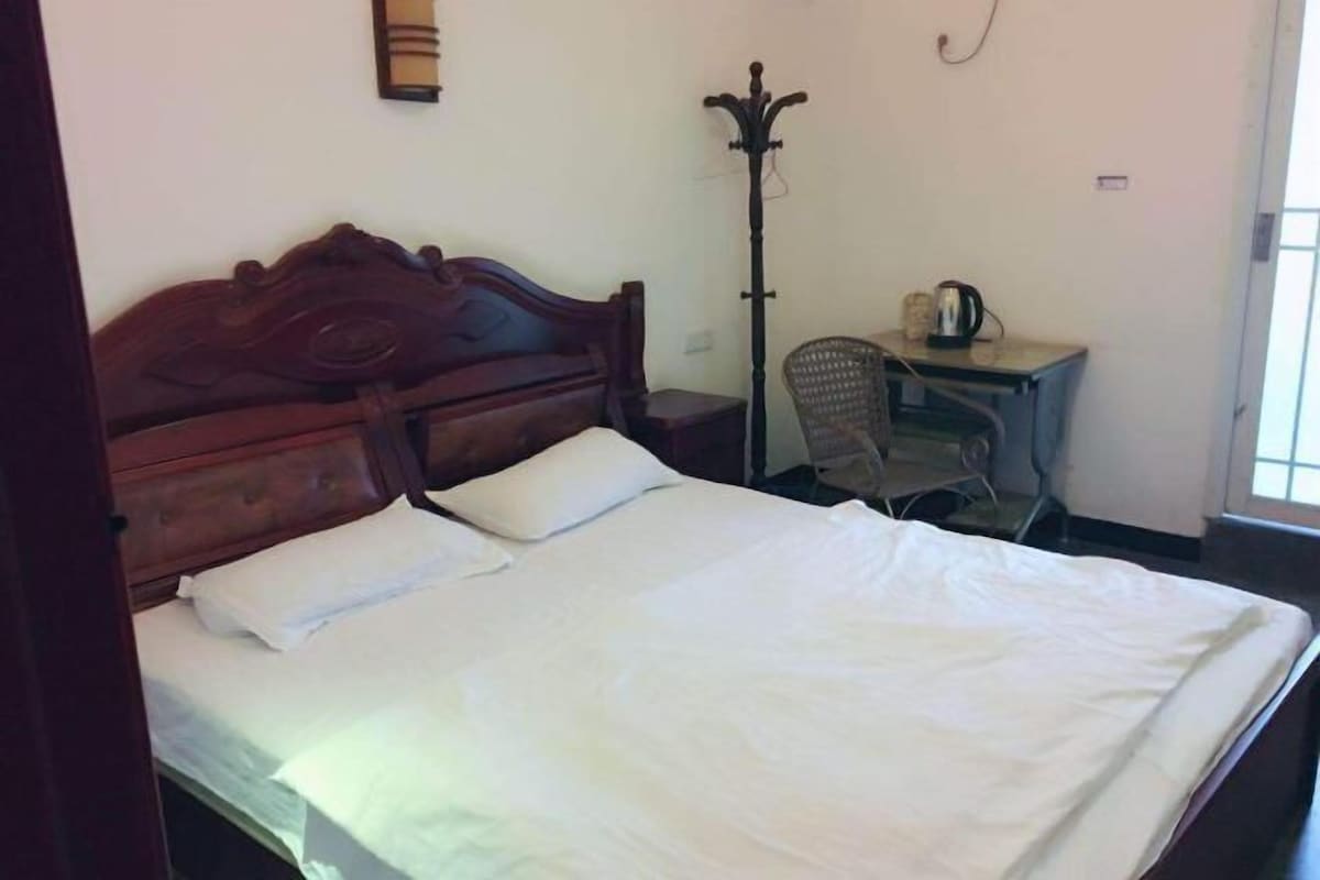 A single bed with a wooden headboard, a small bedside table with a kettle, and a chair.