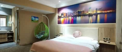 Een hotelkamer met een bed, een hangstoel, een schilderij van een stadsgezicht en een badkamer met een spiegel en wastafel.