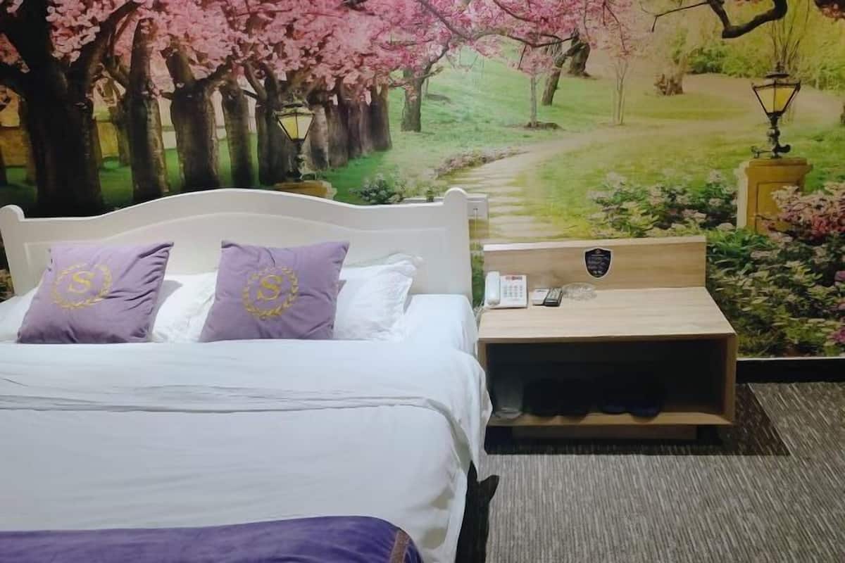 A hotel room with a bed, two purple pillows, a nightstand with a phone, and a wall mural of a garden.