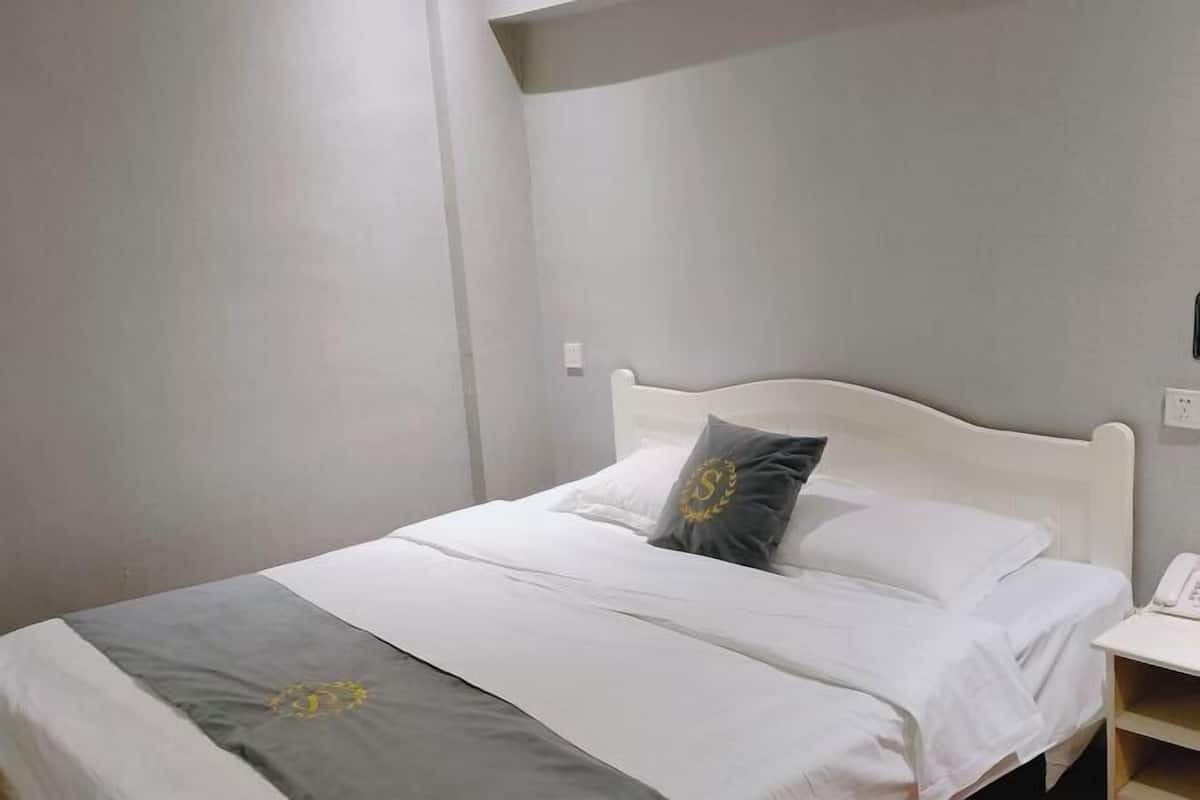 A neatly made bed with a grey and white bedspread, a white headboard, and a bedside table with a telephone.
