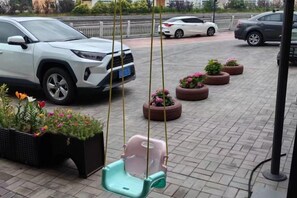 Un estacionamiento con una camioneta SUV blanca, una silla colgante y macetas con flores.