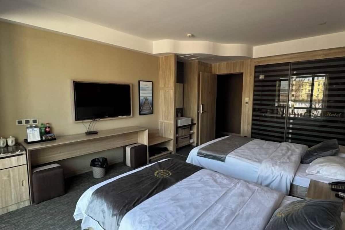 A hotel room with two beds, a TV, a desk, and a window with blinds.