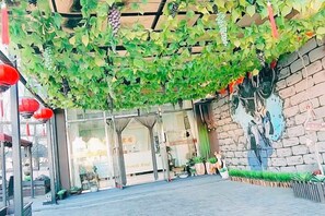Fachada con entrada cubierta de hiedra verde, un mural en la pared y un escaparate de vidrio transparente.