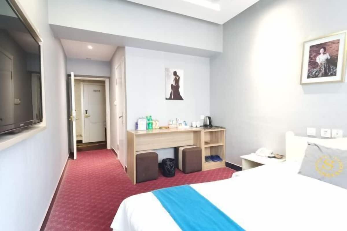A hotel room with a bed, a desk, a chair, a wardrobe, and a door leading to another room.