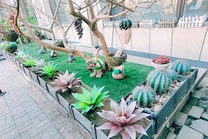 Un jardín con diversas plantas y elementos decorativos, incluyendo un árbol con adornos colgantes y un pequeño estanque.