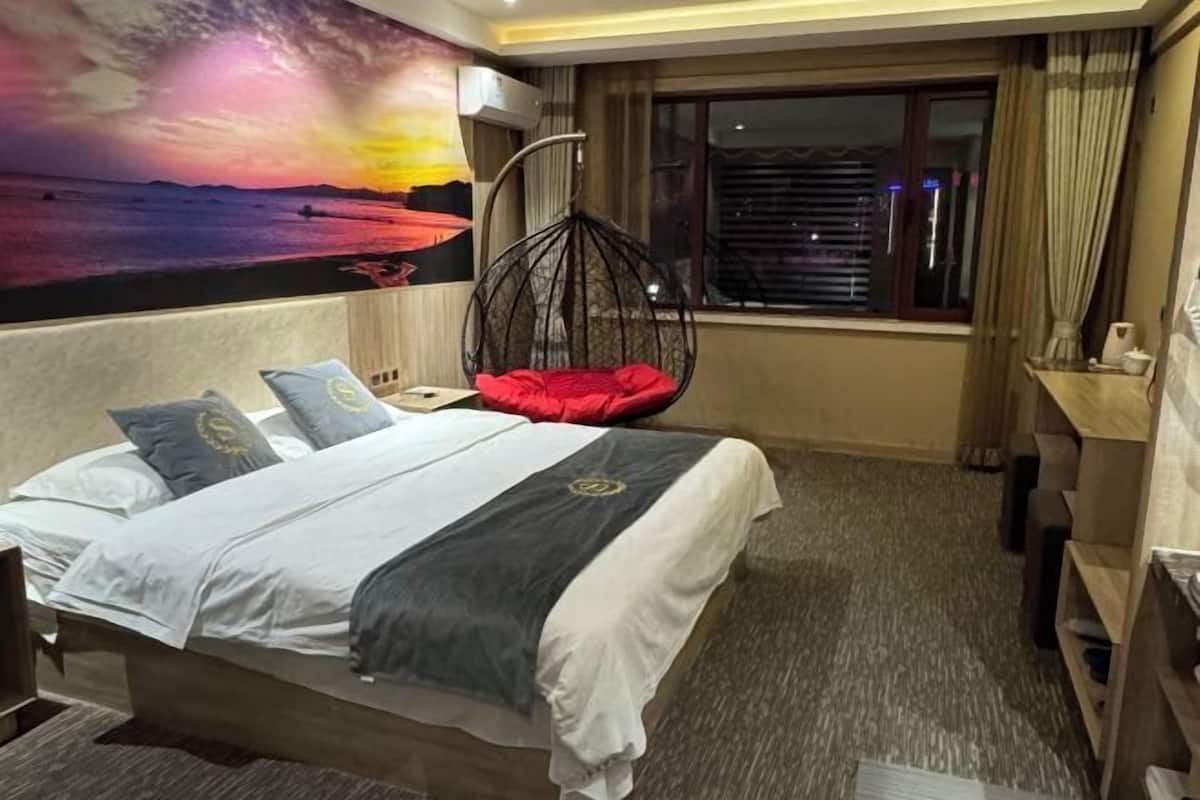 A hotel room with a bed, a hanging chair, a large window, and a wall mural.