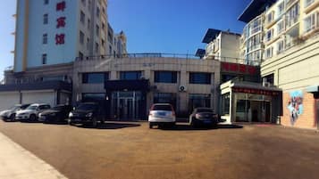 A hotel with multiple floors, a parking lot with several cars, and a clear blue sky.