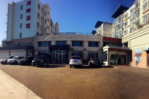 A hotel with multiple floors, a parking lot with several cars, and a clear blue sky. - Riverside Hotel (Dalian)