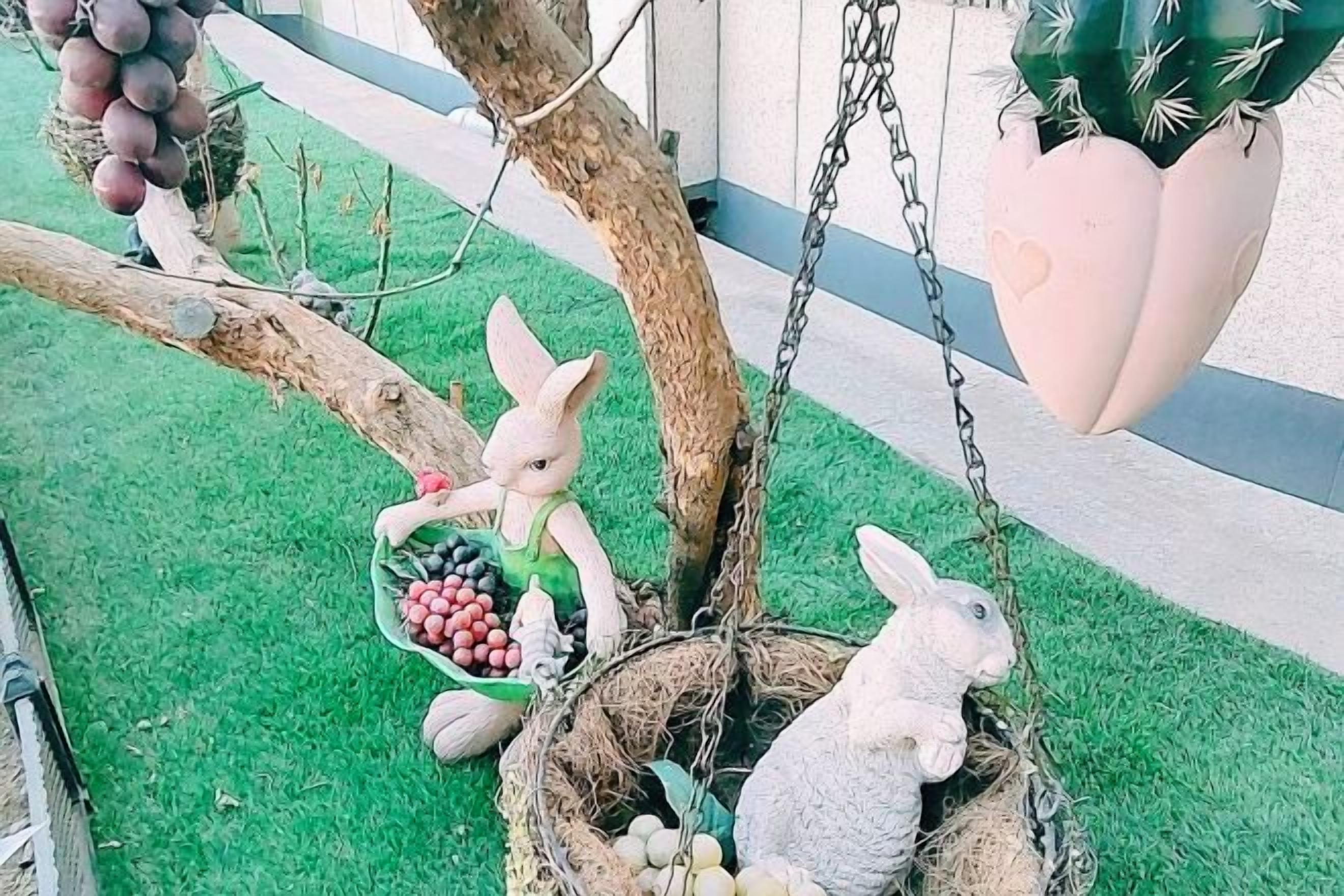 A garden with a tree, a hanging planter, and a decorative rabbit sculpture.