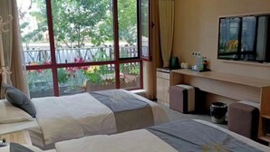 A hotel room with two beds, a TV, a desk, and a view of greenery outside. - Riverside Hotel (Dalian)