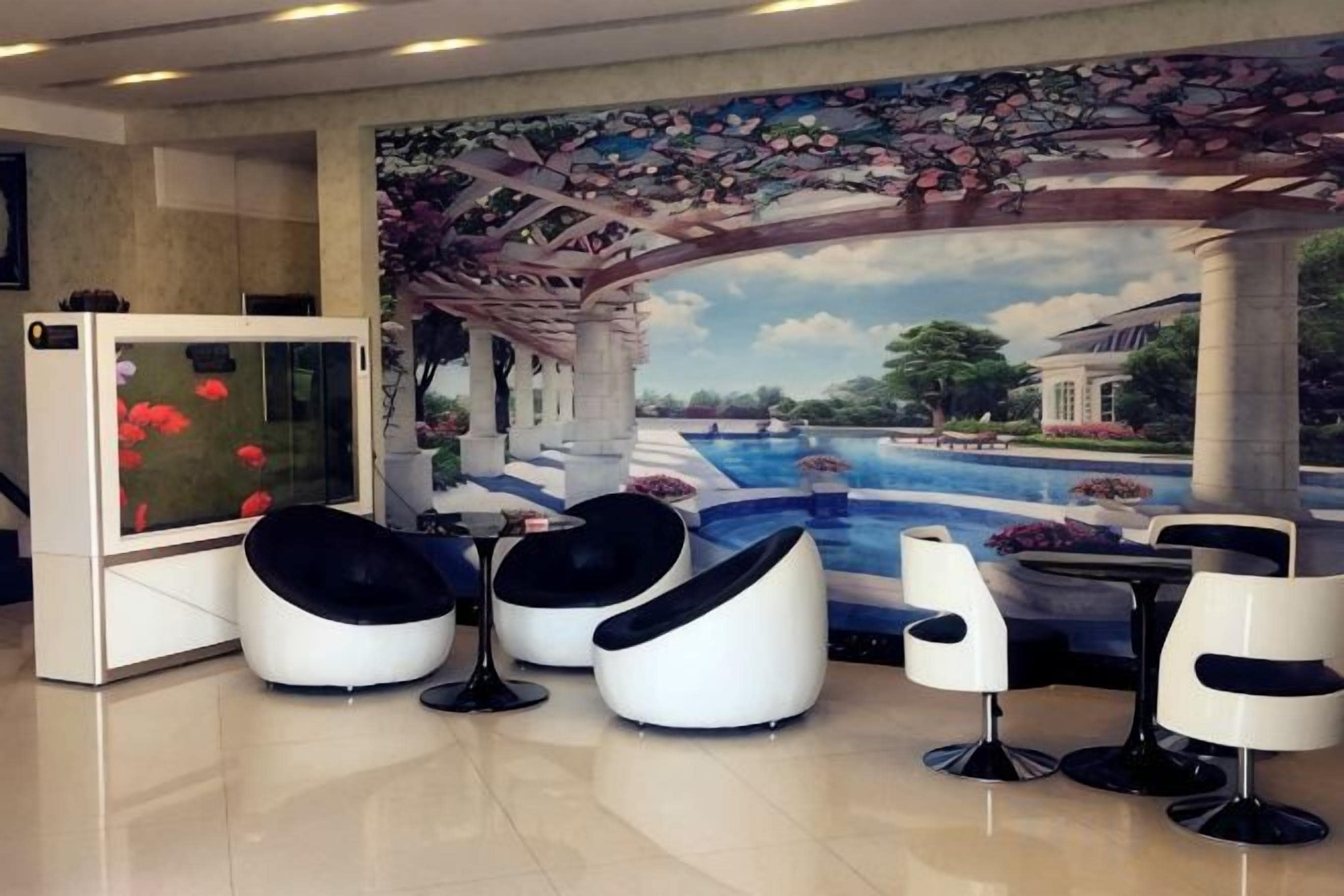 A hotel lobby with a mural of a garden and pool, black and white chairs, and a television.