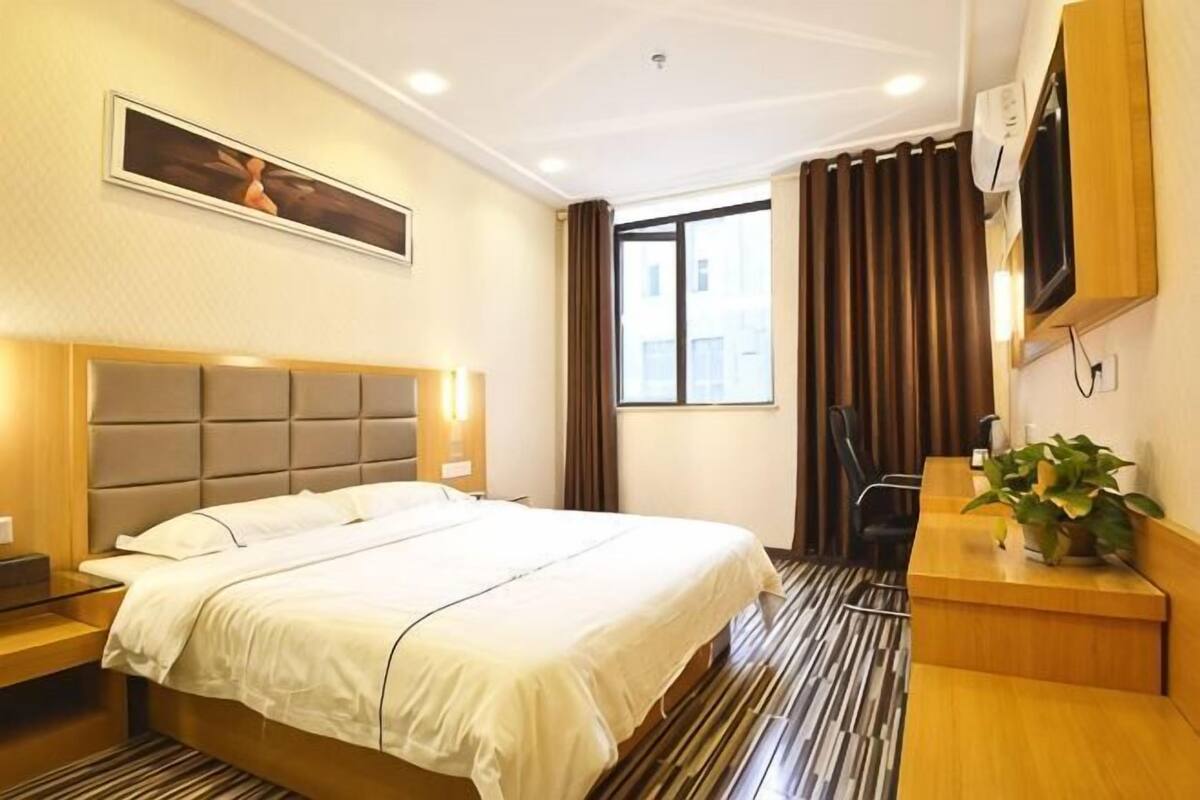 A hotel room with a bed, a desk, a chair, a TV, and a window with curtains.