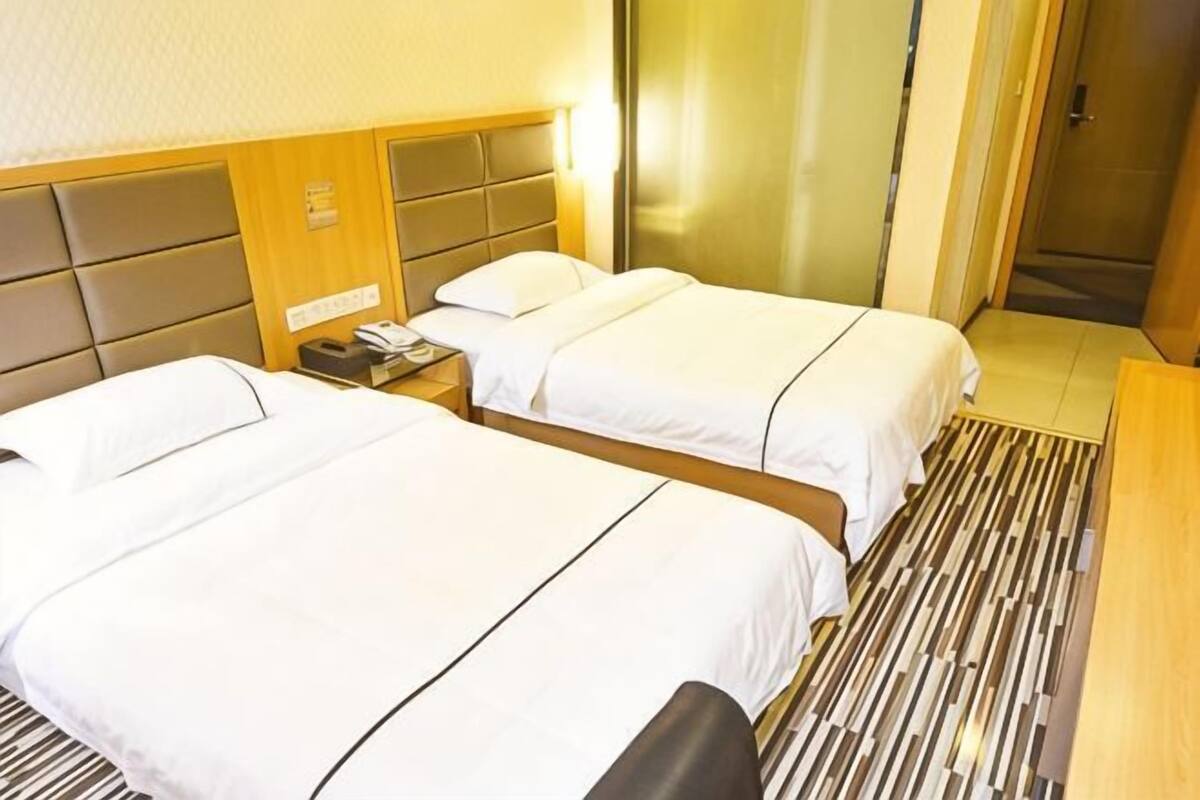 A hotel room with two beds, a wooden headboard, a bedside table with a phone, and a striped floor.