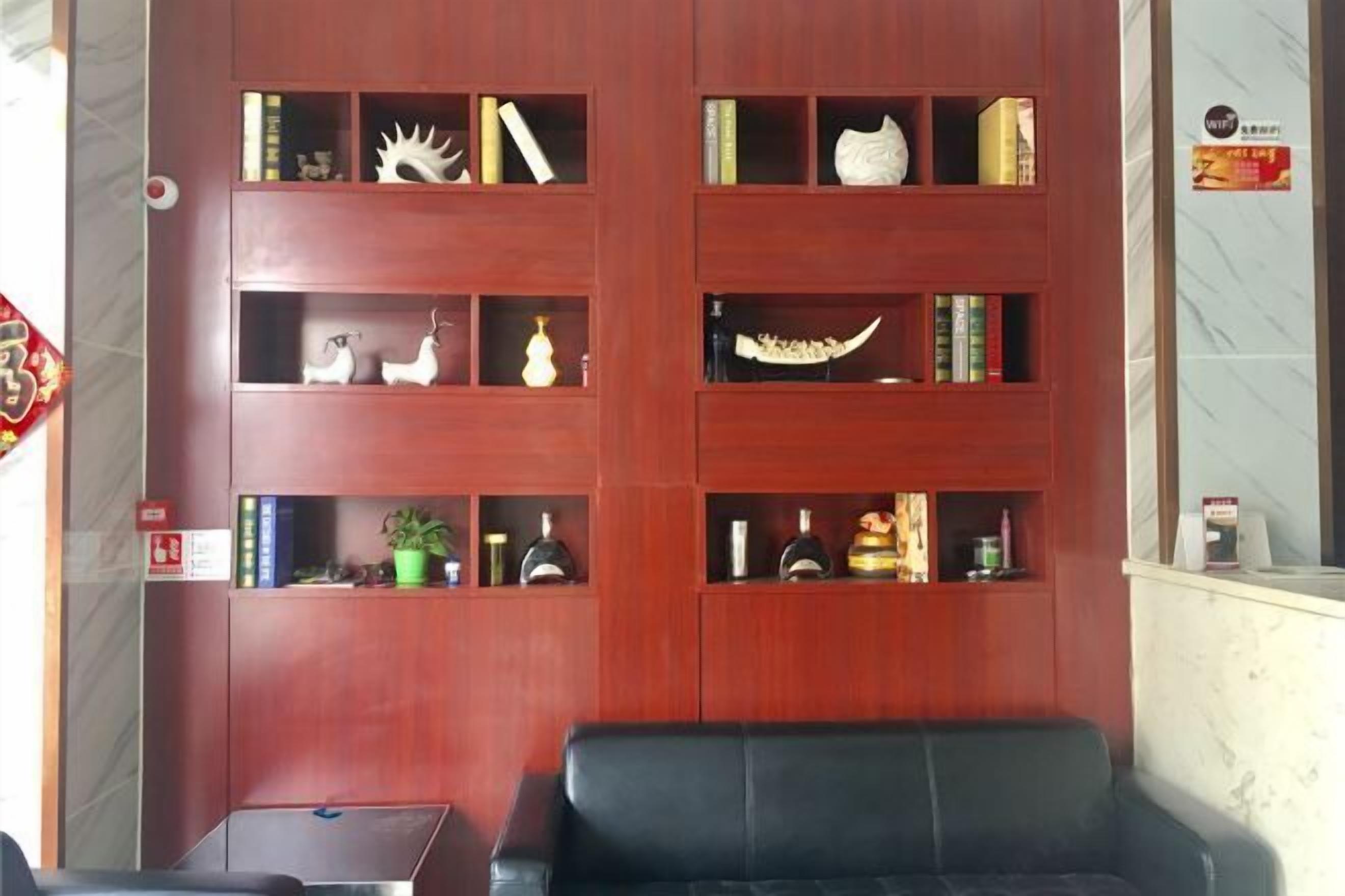 A room with a wooden bookshelf filled with books and decorative items, a black leather sofa, and a small table.