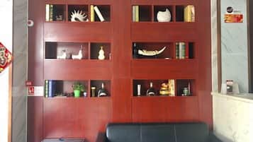 A room with a wooden bookshelf filled with books and decorative items, a black leather sofa, and a small table.