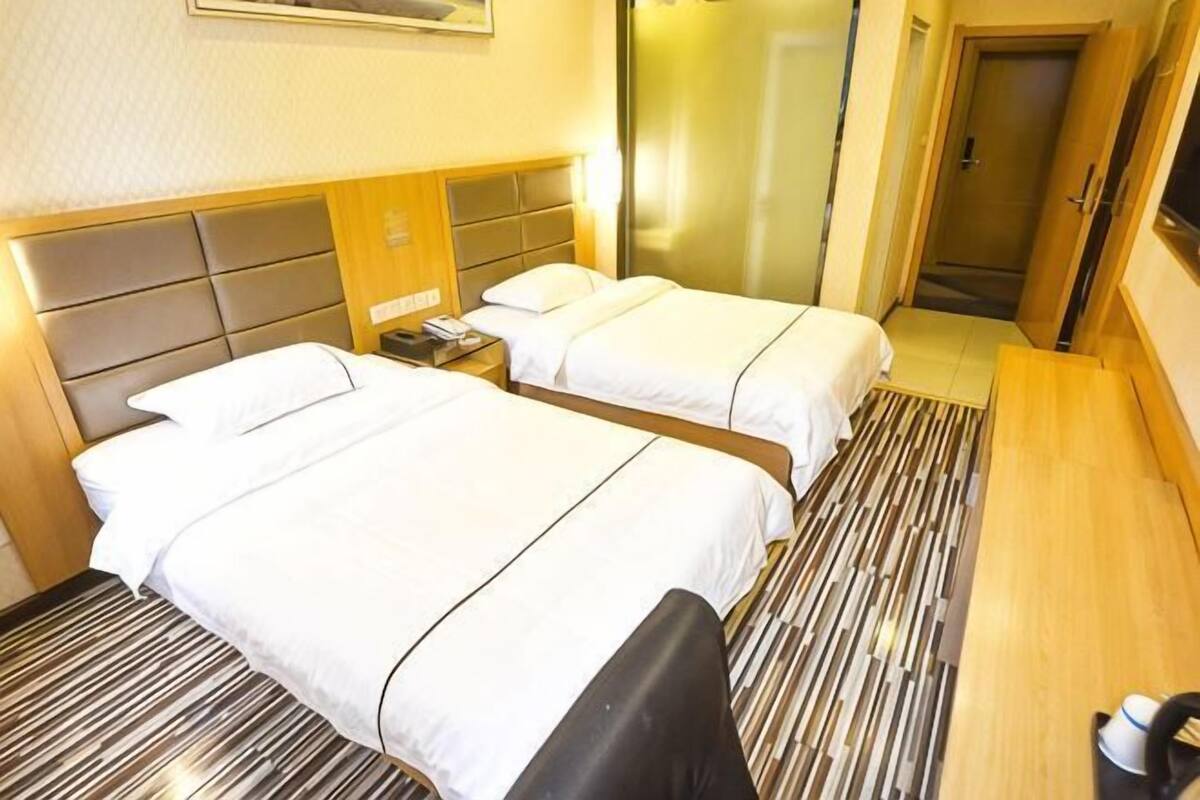 A hotel room with two beds, a wooden headboard, a bedside table with a lamp, and a mirror.