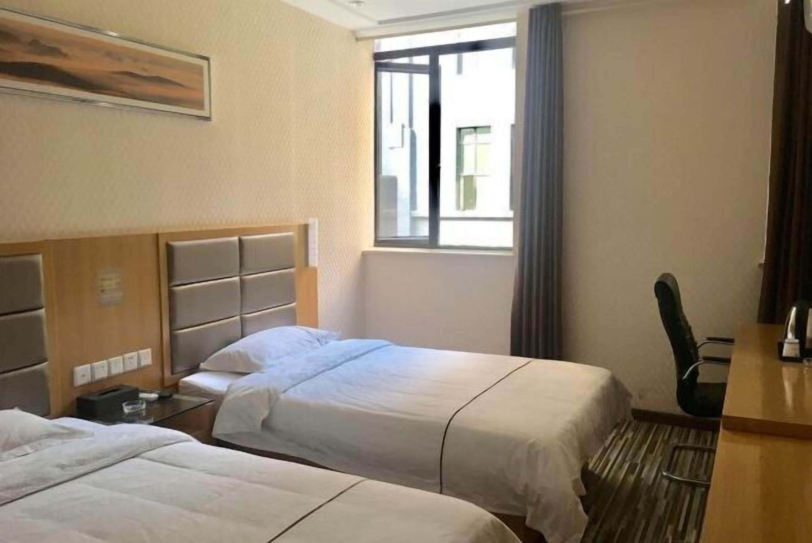 Une chambre d’hôtel avec deux lits, un bureau, une chaise, une fenêtre et un tableau au mur.