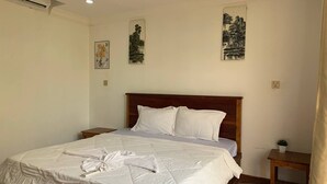 A neatly made bed with white linens and towels, a wooden headboard, and two wall-mounted paintings. - Ratana Bungalow (Kampot)
