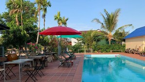 A swimming pool with lounge chairs and tables, surrounded by palm trees and a clear sky. - Ratana Bungalow (Kampot)