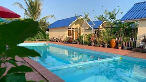 A swimming pool with a clear blue water surface, surrounded by potted plants and a building with a blue roof. - Ratana Bungalow (Kampot)