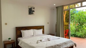 A neatly made bed with white linens and a folded towel, a small bedside table with a plant, and a window with curtains. - Ratana Bungalow (Kampot)