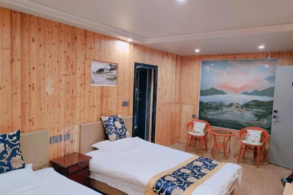 Ein Zimmer mit Holzwandverkleidung, zwei Betten mit weißen Laken, einem Landschaftsbild und zwei kleinen Tischen mit Stühlen.