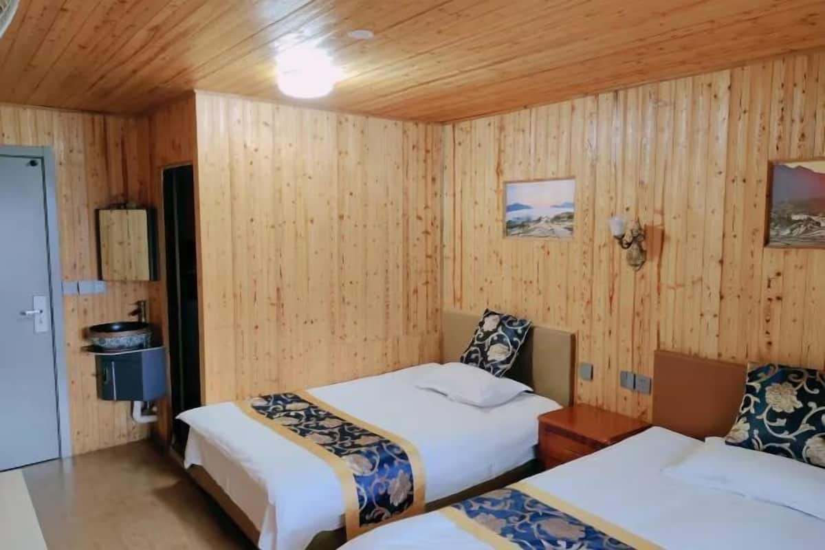 Ein Zimmer mit Holzvertäfelung, zwei Betten mit blumigen Überdecken, einem kleinen Nachttisch, einer wandmontierten Leuchte und einem Gemälde.