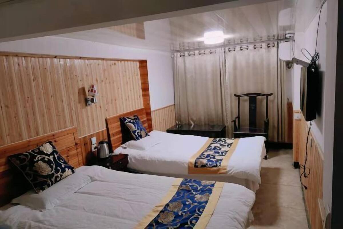 Ein Hotelzimmer mit zwei Betten, einem kleinen Tisch, einem Sessel, einem Fernseher und einem Vorhang.
