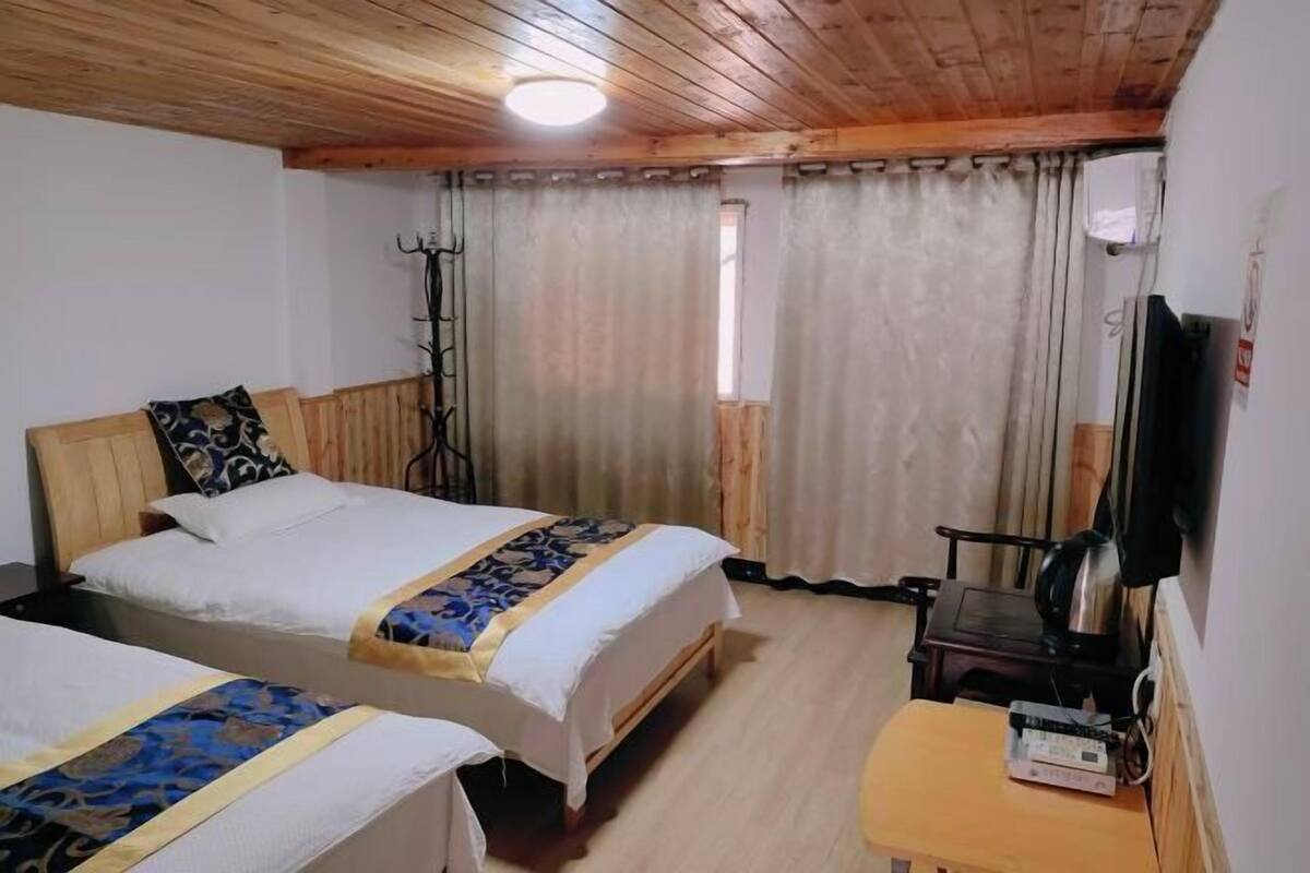 Ein Zimmer mit zwei Betten, einer Holzbalkendecke, einem kleinen Tisch mit Wasserkocher und einem Fernseher an der Wand.