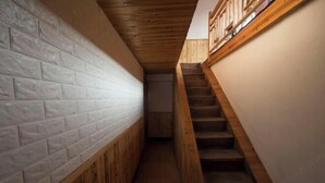 Een smalle gang met een houten trap aan de ene kant en een witte bakstenen muur aan de andere kant.