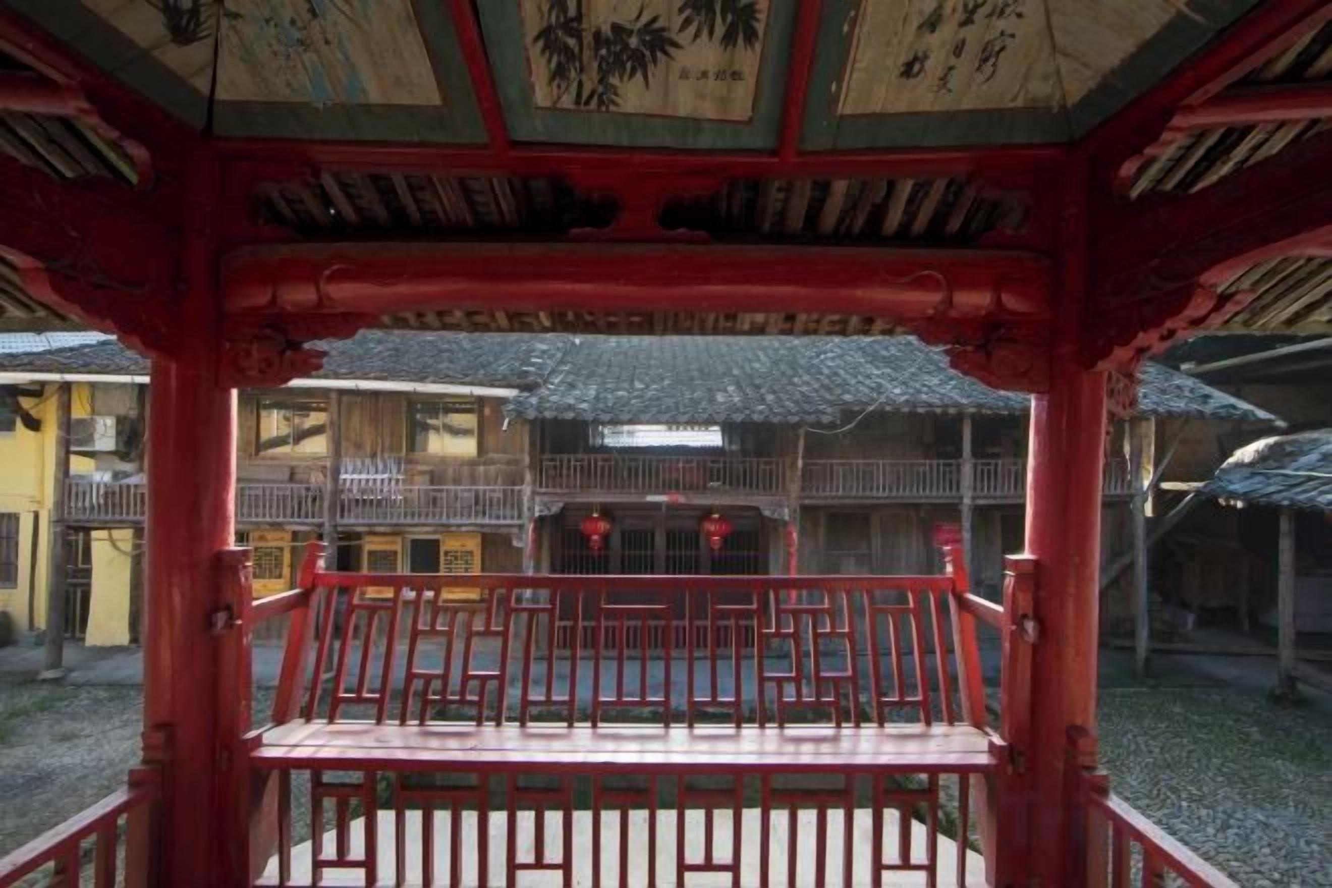 Un edificio tradicional japonés con estructura de madera roja, un balcón con barandilla y vistas a la arquitectura circundante.