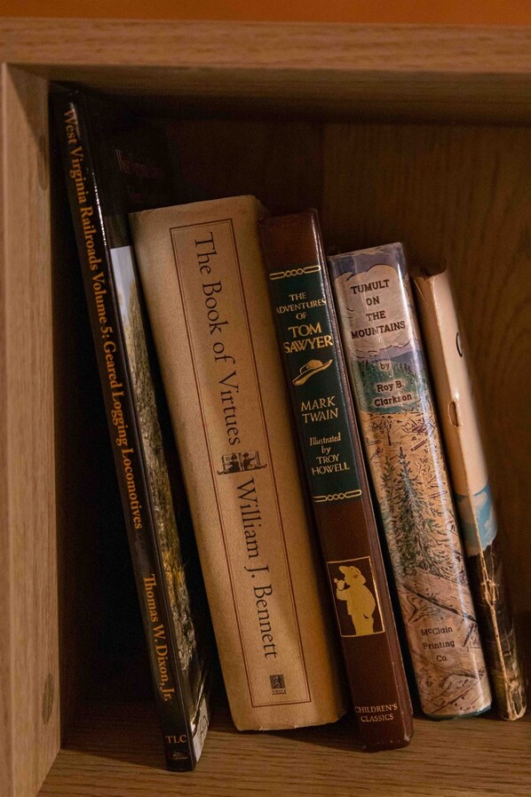 Ein Holzbücherregal mit mehreren Büchern, darunter 'The Book of Virtues' von William J. Bennett, 'The Adventures of Tom Sawyer' von Mark Twain und 'Tumult on the Mountains' von Roy B. Clarkson.