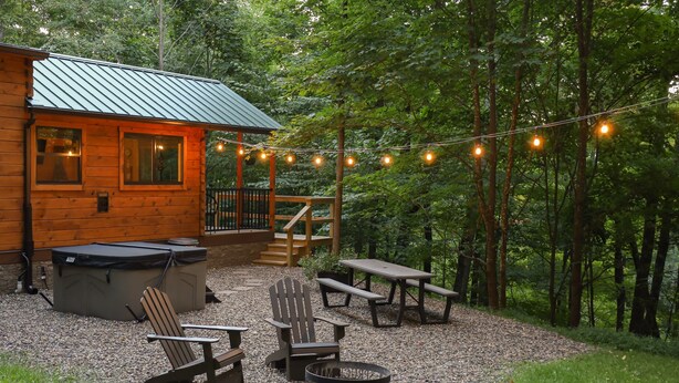 Een houten vakantiehuisje met een terras, buitenmeubels en een vuurkuil.
