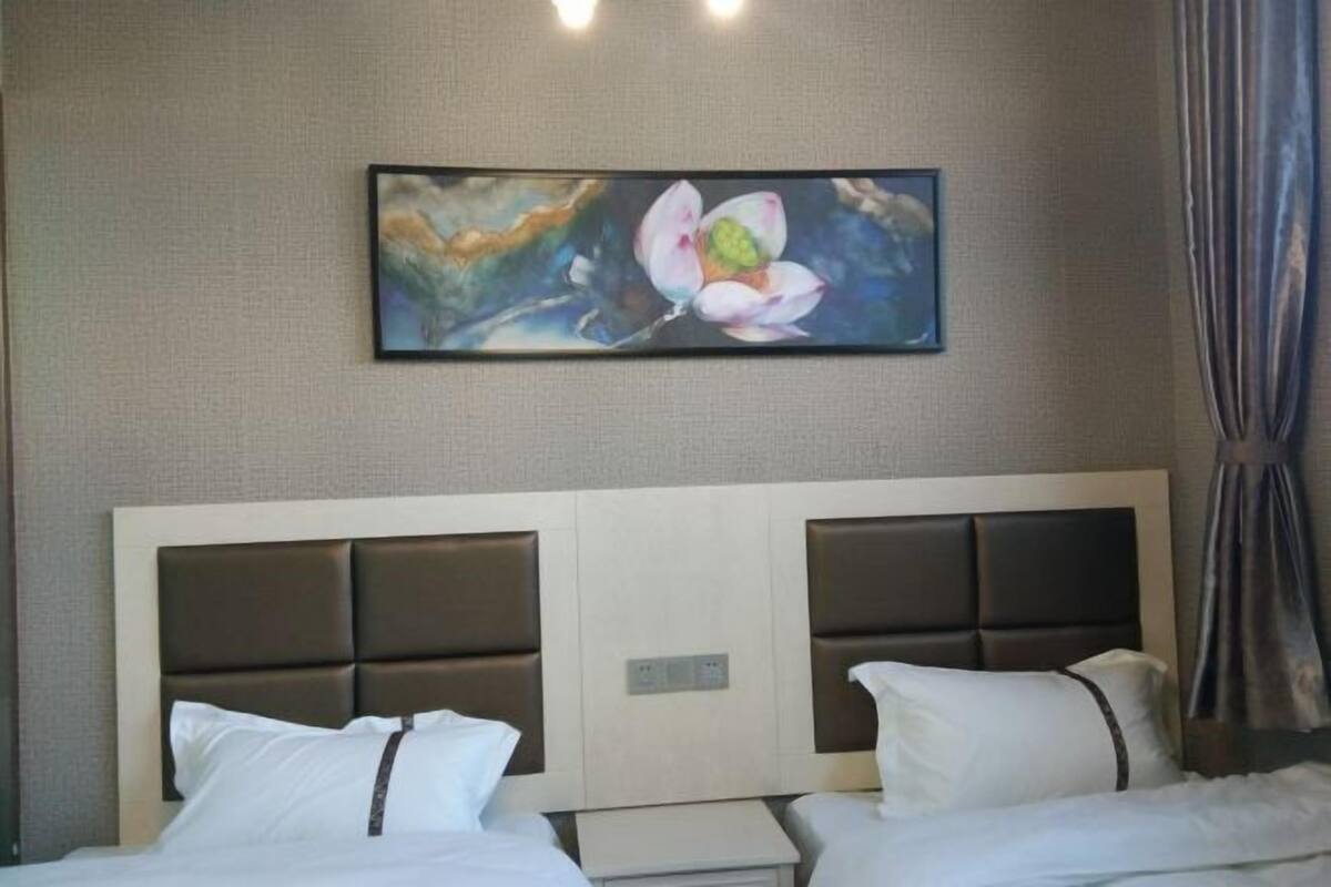 A hotel room with a large bed, a nightstand, and a painting of a flower on the wall.