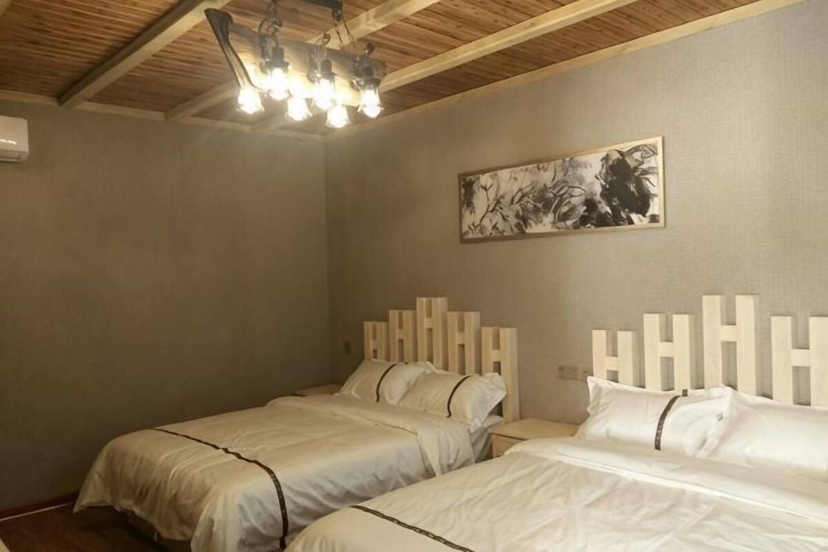 A room with two beds, a wooden ceiling, a wall-mounted light fixture, and a framed picture.