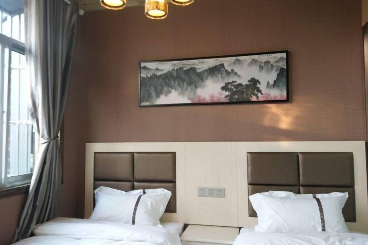 A hotel room with two beds, a large painting of mountains, and a window with curtains.