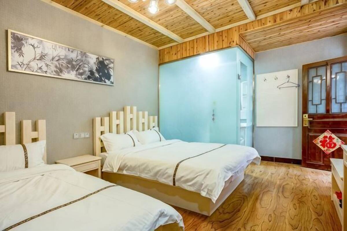 A bedroom with two beds, a wooden ceiling, a wall-mounted artwork, a wardrobe, and a door with a decorative emblem.