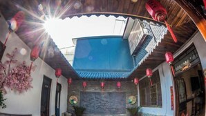 A traditional courtyard with a tiled floor, a stone wall with a mural, and red lanterns. - Anyu · Wooden House (Zaozhuang)