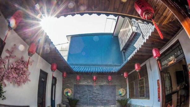 A traditional courtyard with a tiled floor, a stone wall with a mural, and red lanterns. - Anyu · Wooden House (Zaozhuang)
